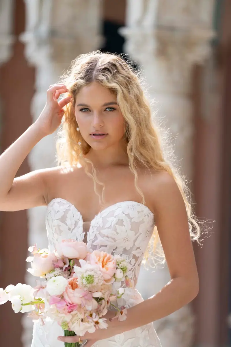 Bride in a strapless Abella gown with a floral appliqué lace bodice, holding a peach and blush bouquet