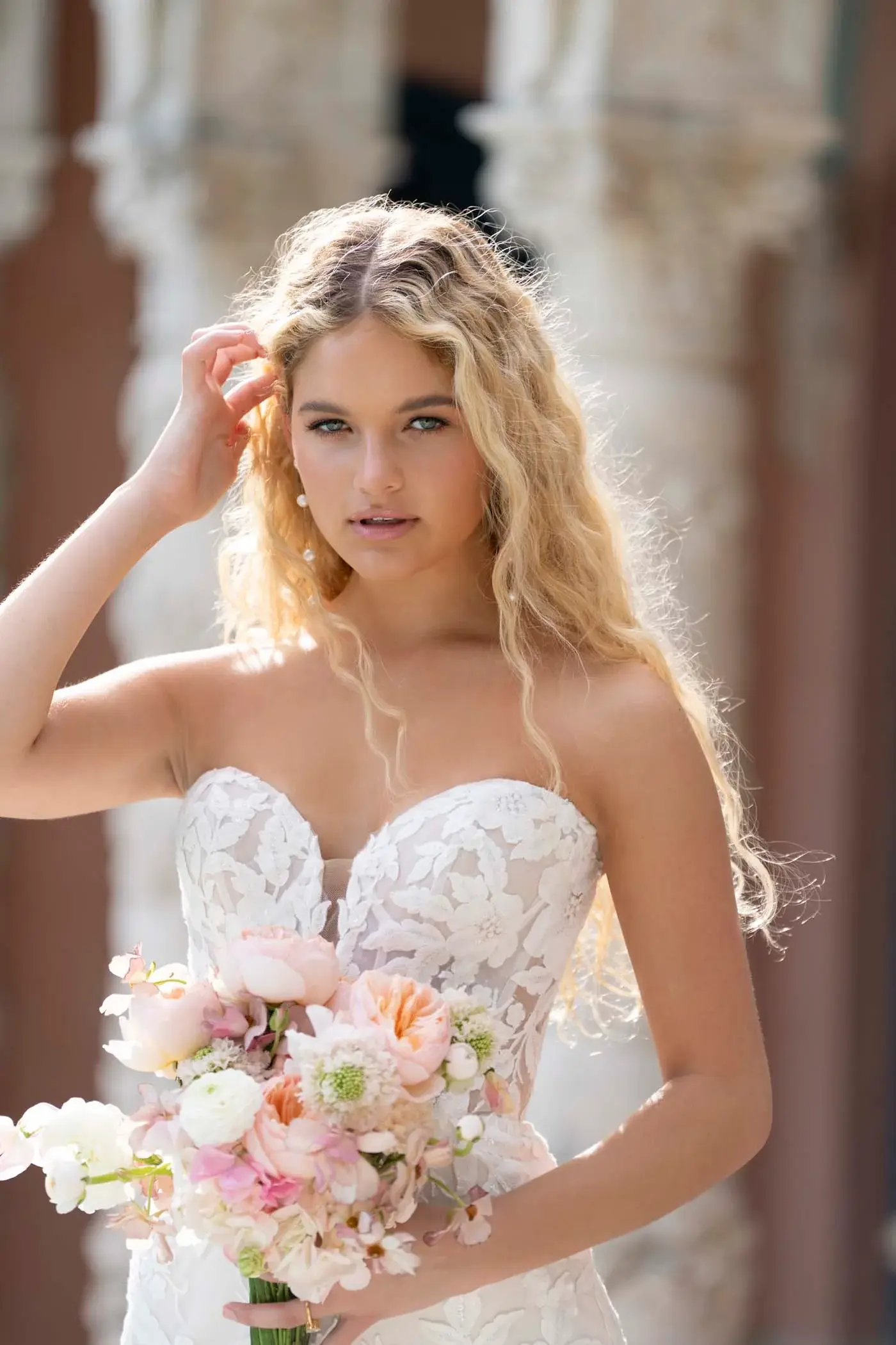 Bride in a strapless Abella gown with a floral appliqué lace bodice, holding a peach and blush bouquet