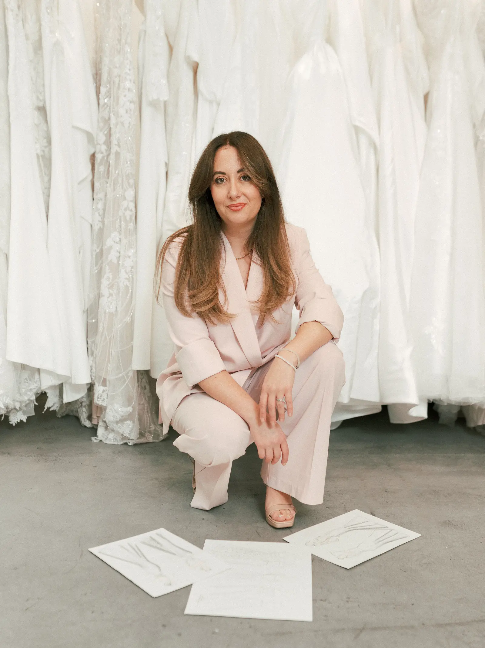 Adriana Garcia at Cande Bridal Boutique working through gown design sketches spread across a table