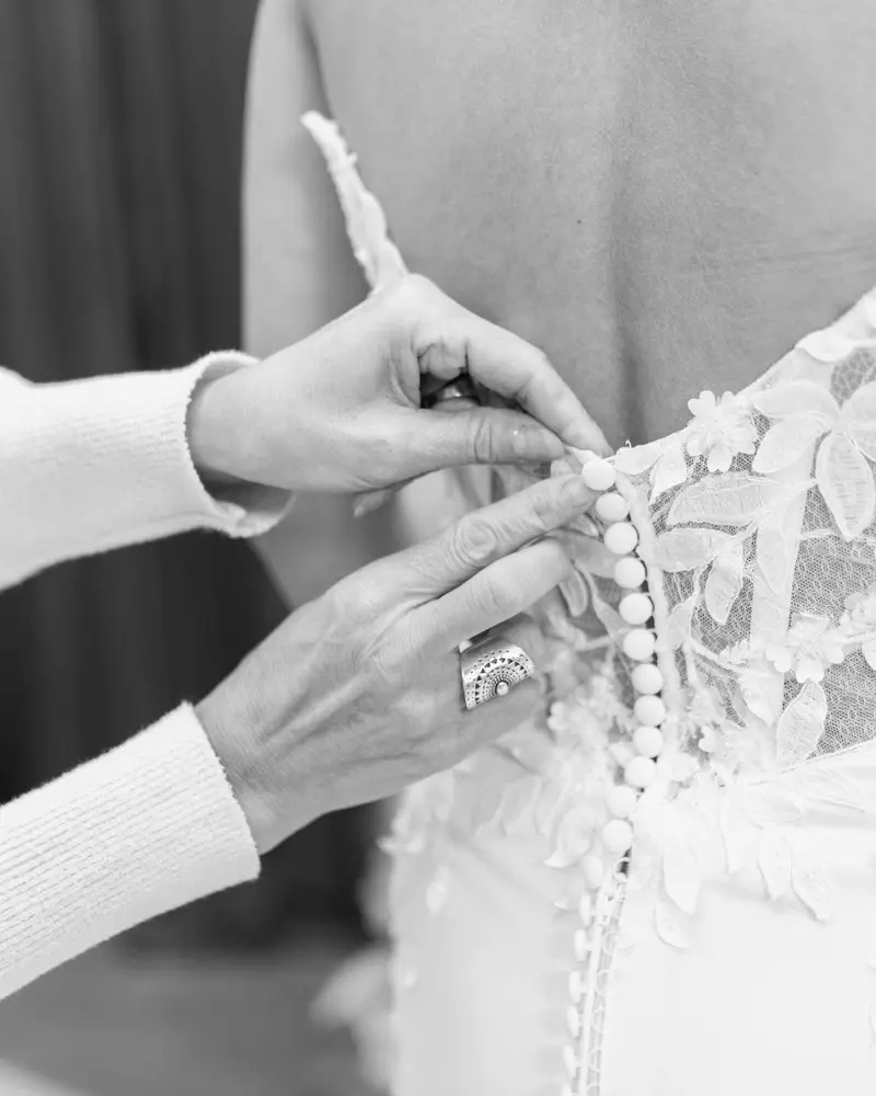 Close detail of covered satin buttons being fastened down the back of a wedding gown