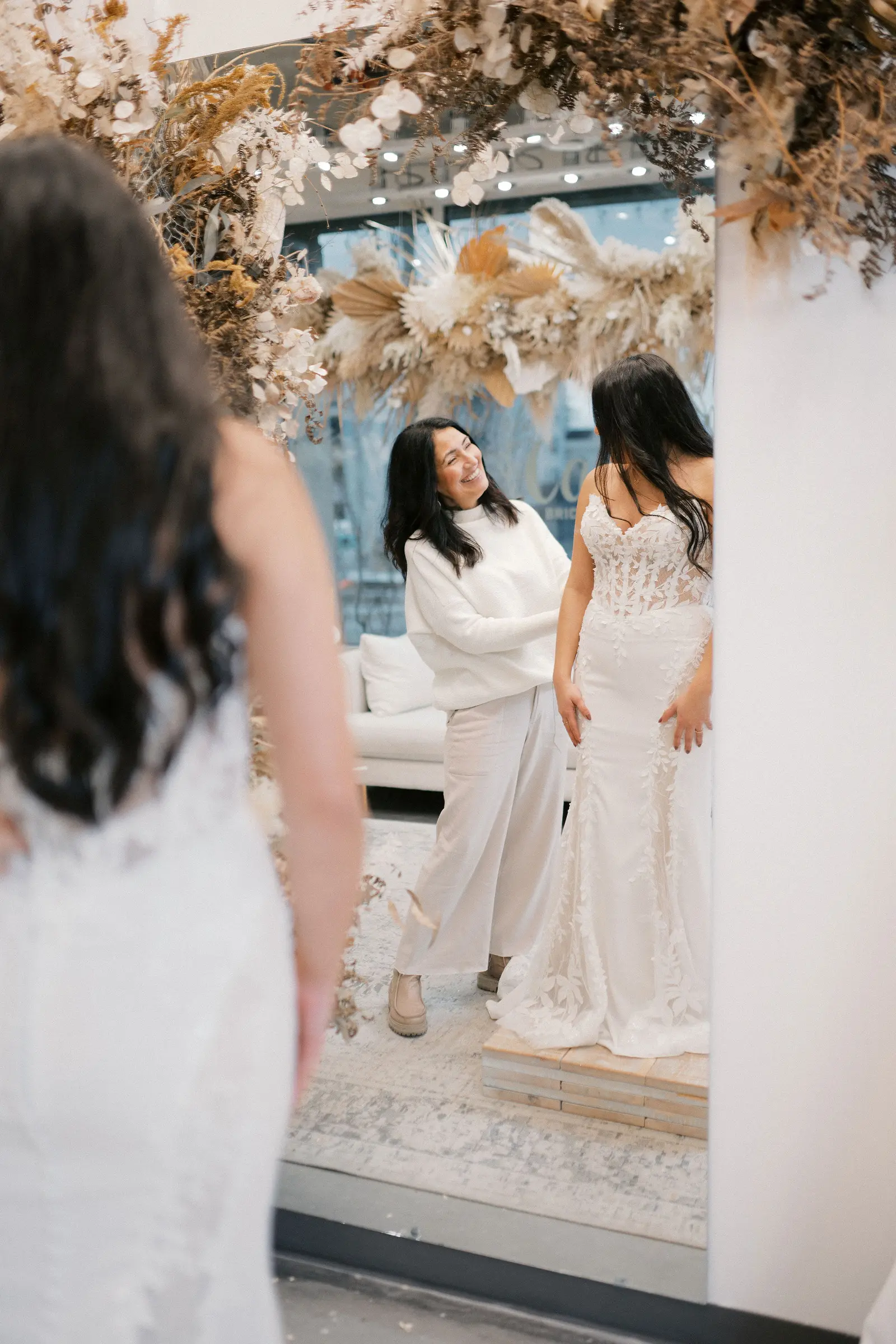 A stylist and a bride in an appointment at Cande Bridal Boutique, a gown held up against the light