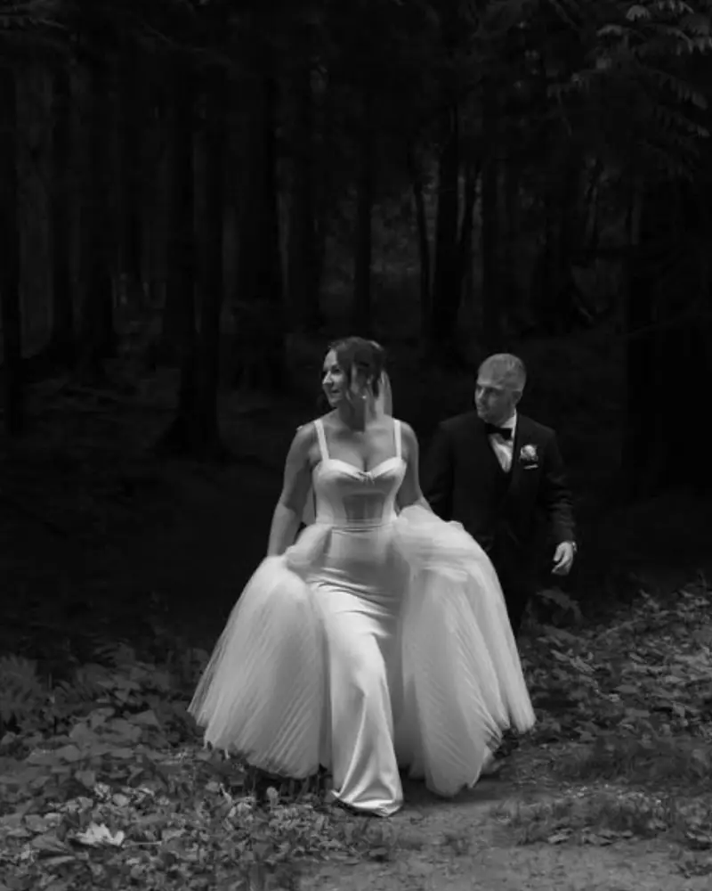 A Cande Bridal Boutique bride in her wedding gown standing among evergreen trees after her ceremony